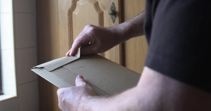 Man opening unboxing cardboard envelope parcel adhesive seal