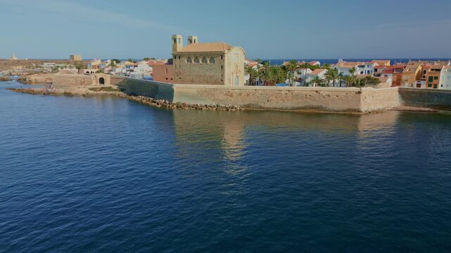 Drone flying backwards from the historic fortified walls of Tabarca island with a small motorboat cruising in the blue mediterranean sea near Alicante, Spain - stock video