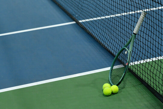 Tennis Racket and Yellow Balls Leaning Against Net on Blue and Green Hard Court