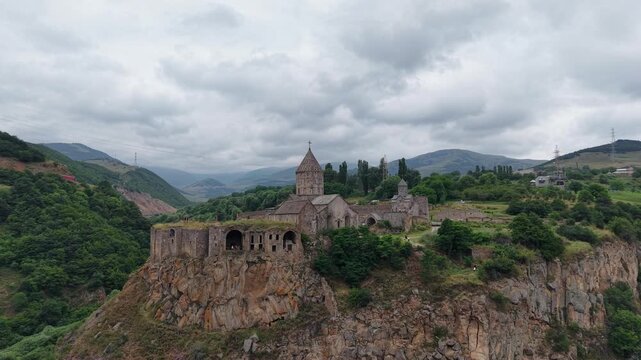 4K Drone Flight Over Tatev Monastery on a Rocky Cliff in Armenia Surrounded by Green Mountains and Dramatic Clouds.