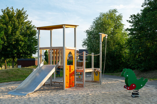 Outdoor empty children playground featuring a stainless steel slide tower, wooden structure, and a green dinosaur spring rocker on sand
