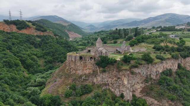 4K Drone Flight Over Tatev Monastery on a Rocky Cliff in Armenia Surrounded by Green Mountains and Dramatic Clouds.
