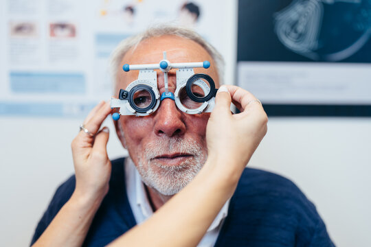 Optometrist adjusting trial lenses on a mature male patient's face during a comprehensive vision checkup and eye clinic consultation.