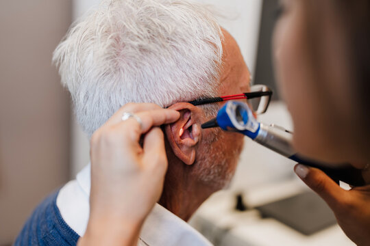 Medical professional checking hearing health and ear canal of an elderly male patient using specialized diagnostic equipment in a clinical setting.