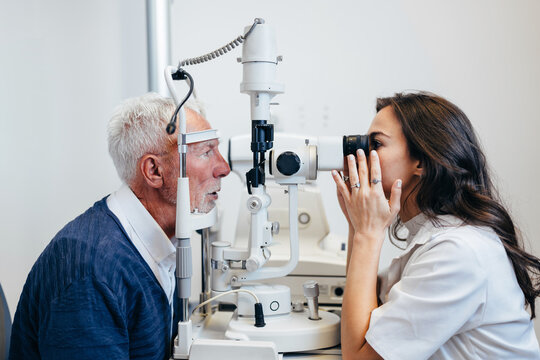 Professional ophthalmologist performing an eye test on an elderly man using specialized medical diagnostic equipment in a bright medical office.