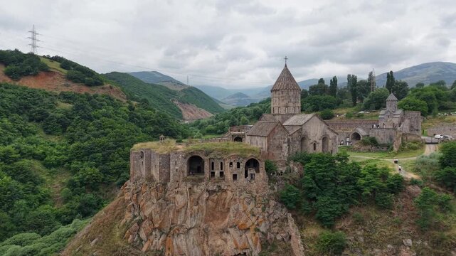 4K Drone Flight Over Tatev Monastery on a Rocky Cliff in Armenia Surrounded by Green Mountains and Dramatic Clouds.