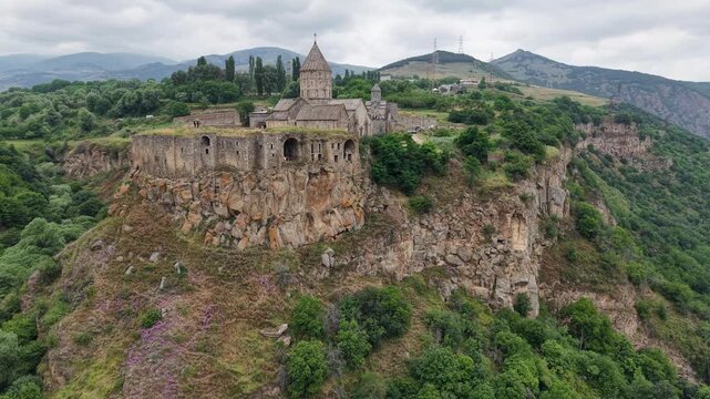 4K Drone Flight Over Tatev Monastery on a Rocky Cliff in Armenia Surrounded by Green Mountains and Dramatic Clouds.