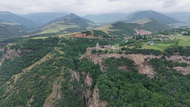 4K Drone Flight Over Tatev Monastery on a Rocky Cliff in Armenia Surrounded by Green Mountains and Dramatic Clouds.