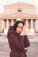Fototapeta premium Woman in maroon coat standing in Moscow with Christmas lights, building in background. Winter holiday concept with decoration.