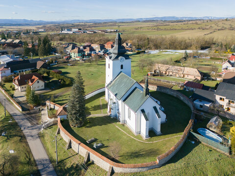Aerial view of the Roman Catholic Church of All Saints enclosed by a historic stone wall, set amidst the rural landscape of the village of Ocova, Banska Bystrica Regio, Slovakia.
