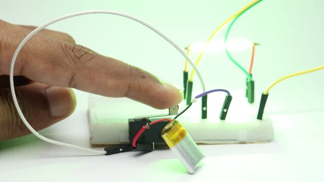 Limit switch on a breadboard circuit turns on a green led filament powered by a small lithium polymer battery