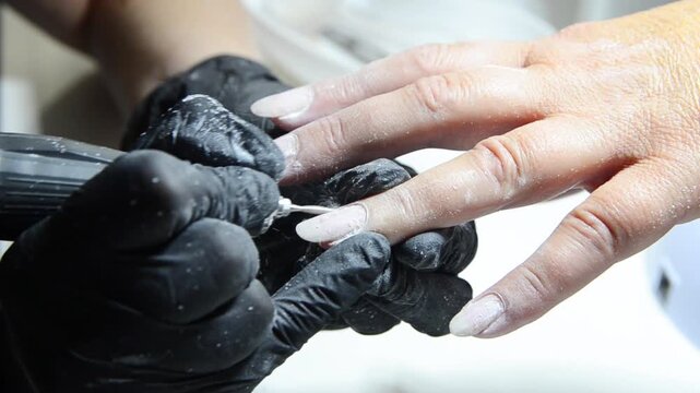 Professional manicurist removing cuticle with an electric nail drill during a hardware manicure. Close-up of nail preparation and cuticle care in a beauty salon.