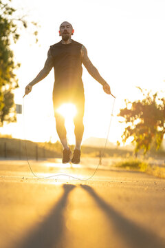 Man jumps rope in early morning light while running on a quiet road surrounded by trees