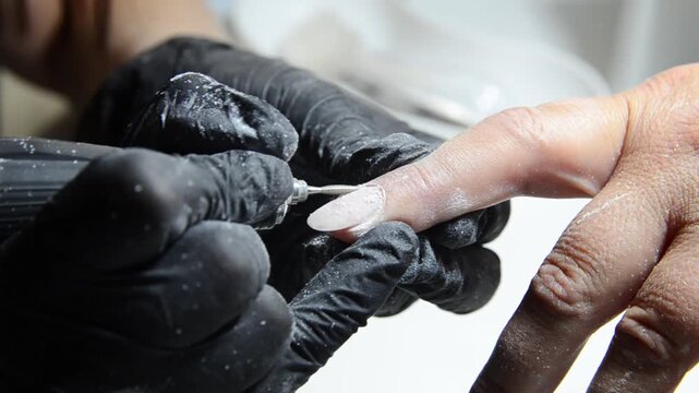 Professional manicurist removing cuticle with an electric nail drill during a hardware manicure. Close-up of nail preparation and cuticle care in a beauty salon.