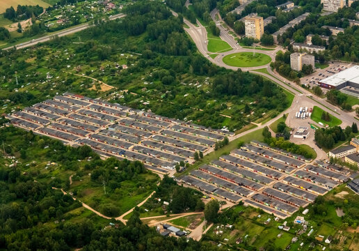 Aerial view of a large garage complex with rows of metal doors surrounded by lush greenery, nearby roads, and residential buildings in Elektrenai, Vilnius County, Lithuania.
