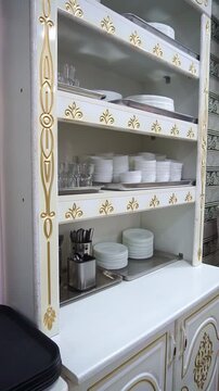 Slow motion camera panning of a classic white kitchen cabinet with gold ornaments and structured shelves for plates and cutlery, vertical video.