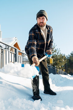 Man, cleaner shoveling snow from sidewalk on sunny winter day