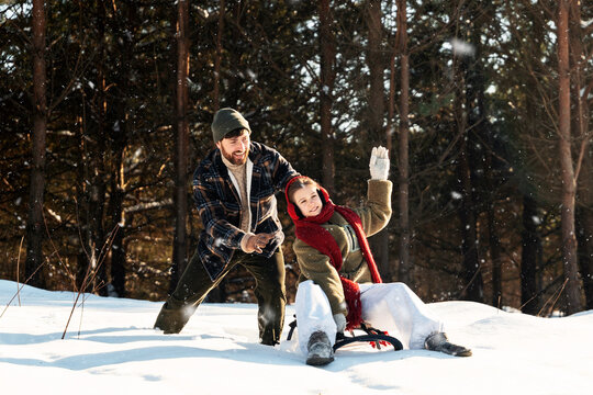 Father and daughter sledging in snowy winter forest
