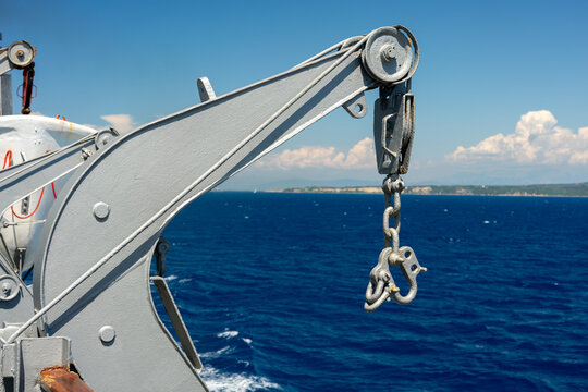 Ship crane mechanism with a large metal hook and heavy chain hanging over the water, showing marine industrial equipment and the deep blue ocean waters landscapes.
