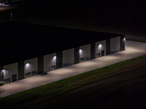 Aerial view of a modern industrial warehouse facility illuminated at night, featuring clean architectural lines and a large paved loading area in Vilnius, Vilnius County, Lithuania.