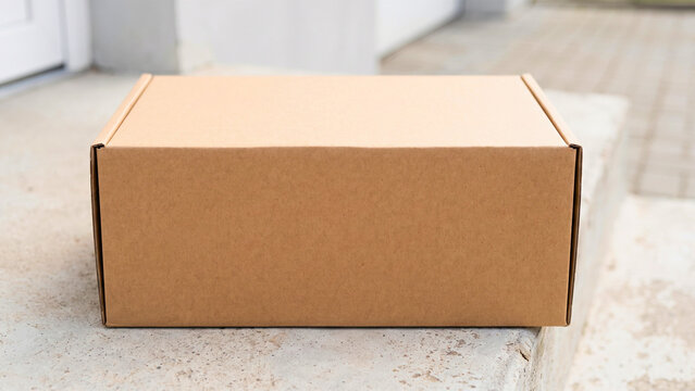 Blank cardboard shipping box on doorstep, e-commerce packaging mockup, delivery marketing display with copy space