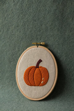 Embroidered pumpkin on linen fabric in wooden embroidery hoop. Handcrafted autumn textile decor for seasonal interior design. Rustic style craftwork for Thanksgiving celebration.