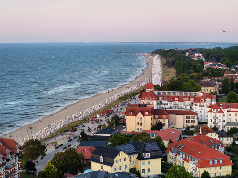Drone view  Ostseebad K&uuml;hlungsborn resort, Baltic beach, promenade, Ferris wheel, hotels, and red roofs at dusk. Calm coastline, beach chairs, seaside tourism, and summer mood shape scenic cityscape