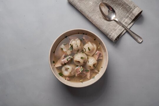 Bowl of Dushbara filled with tiny dumplings in lamb broth, surrounded by steam. Concept of warm, comforting meal experience with rustic appeal and fresh mint flavors.
