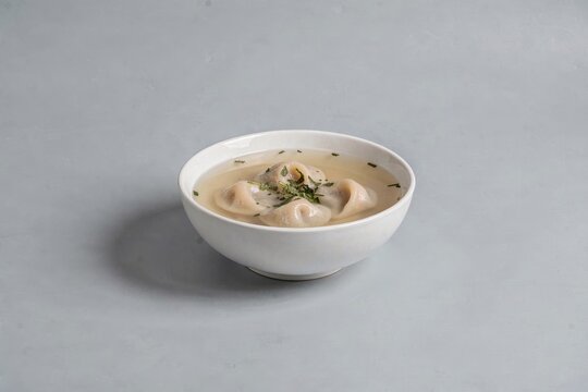 Dushbara, bowl filled with creamy soup topped with tiny dumplings, fresh herbs. Concept of warmth, comfort, inviting atmosphere, tiny dumplings in lamb broth mint.