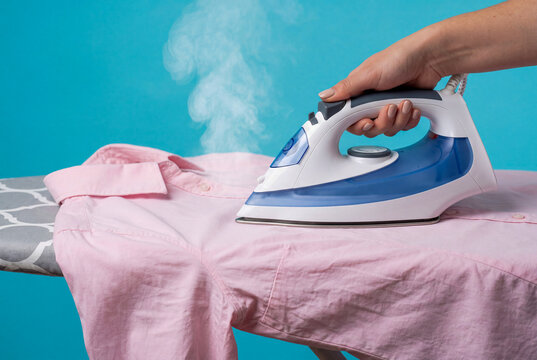 Woman Ironing Pink Shirt with Steam Iron on Blue Background