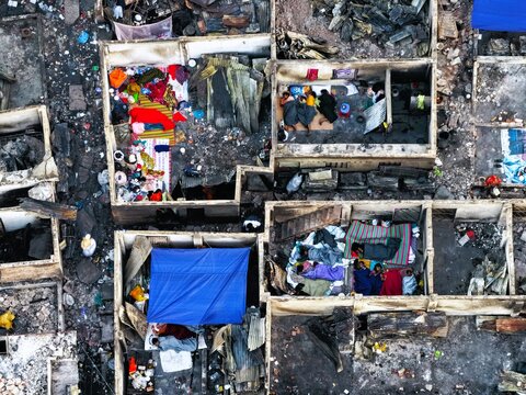Aerial view of Korail Basti showing dense makeshift dwellings with people resting on mats and scattered debris in the aftermath of a fire in Dhaka, Dhaka Division, Bangladesh.