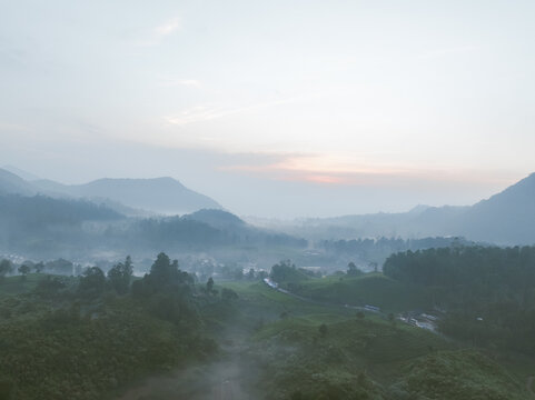 Aerial view of the misty tea plantations and rolling hills in the early morning light in Rancabali, West Java, Indonesia.