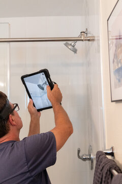 A man at work, an inspector taking a picture of the shower head of a residential home	
