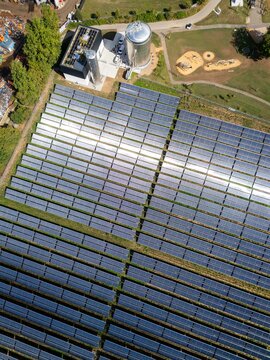 Aerial view of a solar thermal power plant with rows of solar panels, storage tanks, and surrounding greenery in Germany.