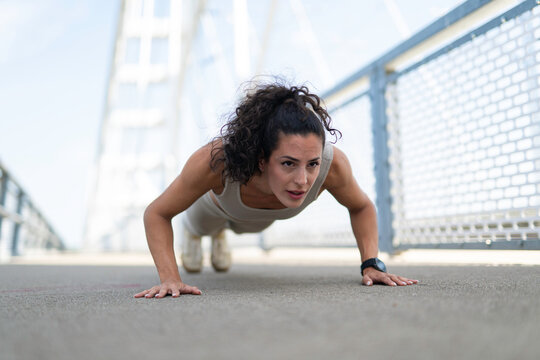 Woman doing pushups outdoors on a bridge during workout