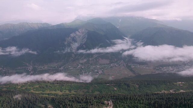 Cinematic drone reveal emerging from mountain peaks over Mestia, Svaneti, Georgia. Stunning aerial view of the alpine valley, historic mountain village and majestic Caucasus Mountains