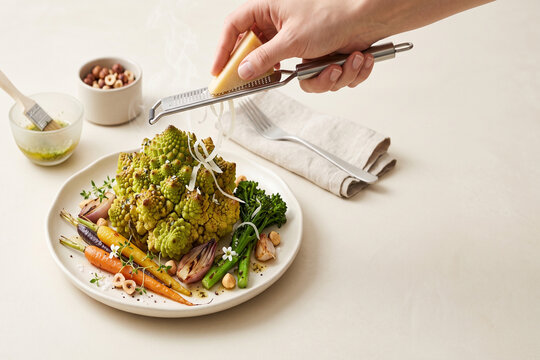 Roasted romanesco broccoli platter with baby carrots, parmesan grater, steam, and hand-grated cheese