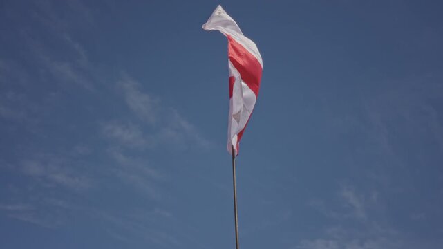England flag bearing red st george cross waving on tall metal pole against clear blue sky above a street corner; national pride unity resilience.