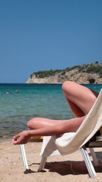 Young woman relaxes on a sun lounger on a sunny beach by the crystal clear sea., a beachgoer resting on a deckchair with a cigarette in his hand. Vertical view.