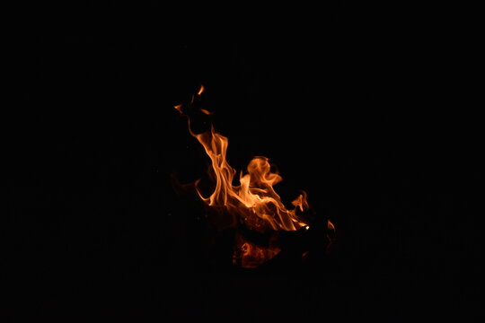 Intense vibrant orange fire flames burning isolated against a dark low-key background in high contrast.