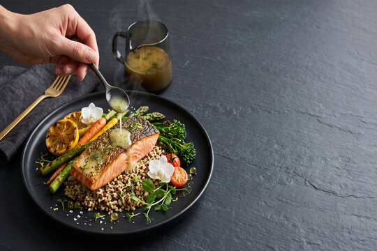 Grilled salmon fillet plate with quinoa asparagus sauce pitcher, spoon, dark background and hand-poured sauce