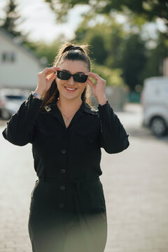 Young woman putting on sunglasses and smiling outdoors