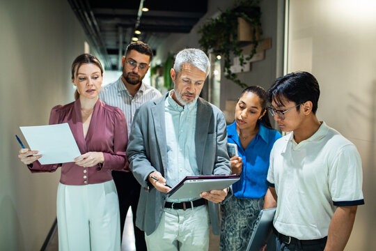 Diverse coworkers reviewing documents in office hallway