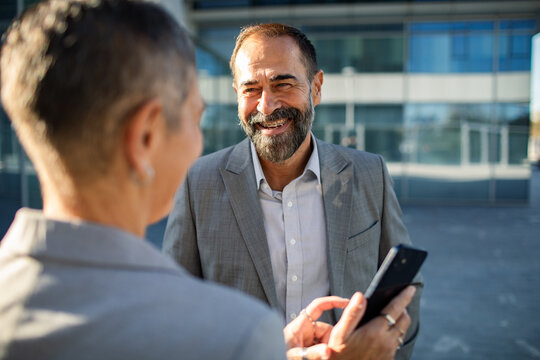 Two business professionals discussing smartphone outside office building