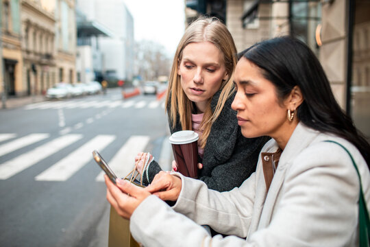 Two women checking smartphone directions on city street