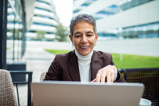 Smiling senior businesswoman working on laptop at modern office campus outdoors