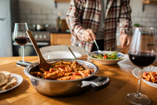 Person serving salad beside pasta in home kitchen