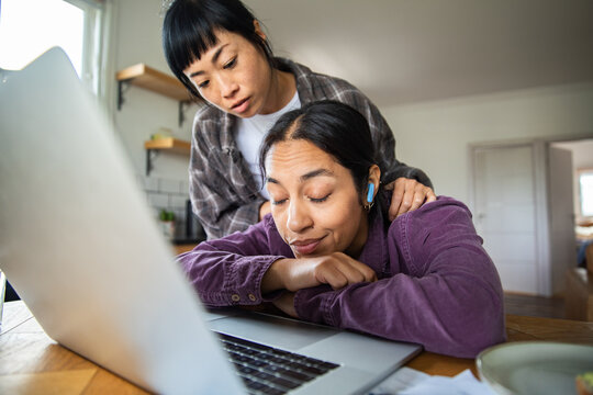Two women offering support at home workspace with laptop
