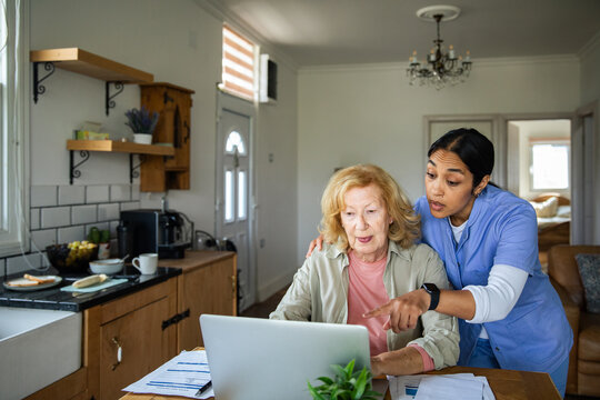 Caregiver helping elderly woman use laptop at home