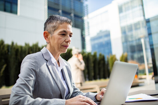 Senior businesswoman working on laptop in urban business district